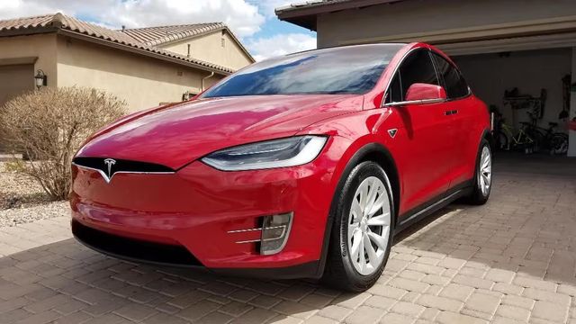 Red Tesla Model Y parked in a driveway outside a suburban house