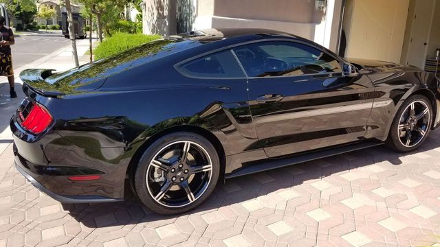 Black sports coupe parked in a driveway beside a house, side view in sunlight