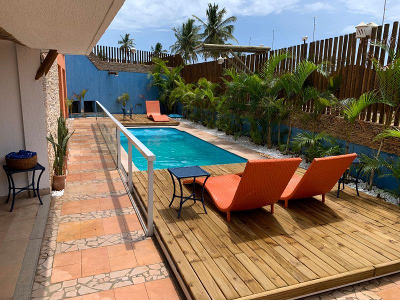 Cena à beira da piscina: piscina, deck de madeira com espreguiçadeiras laranja, parede azul, palmeiras.
