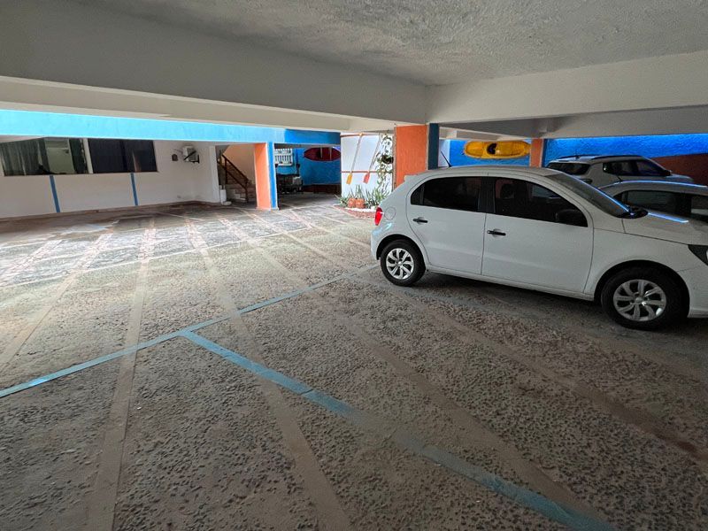 Estacionamento coberto com um carro branco estacionado. Paredes azuis e laranjas.