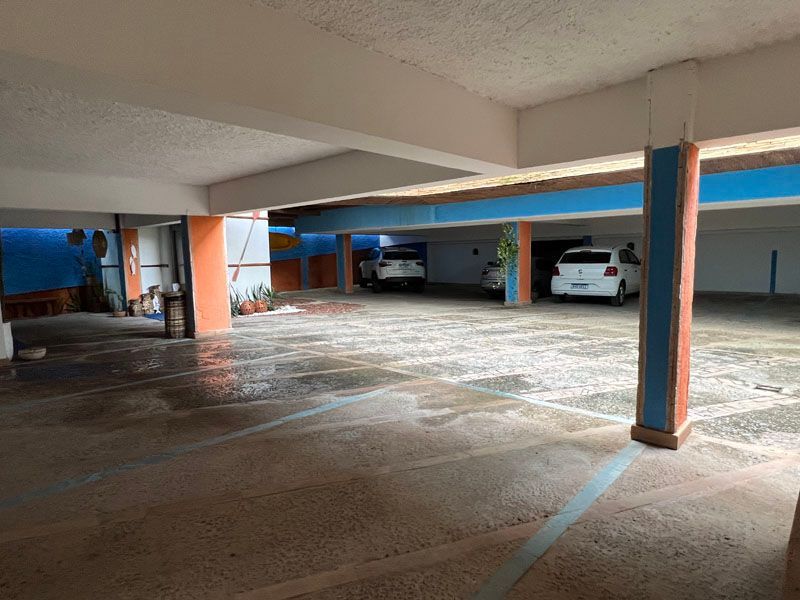 Garagem coberta com dois carros brancos. Piso molhado, colunas azuis e laranjas, vigas no teto.