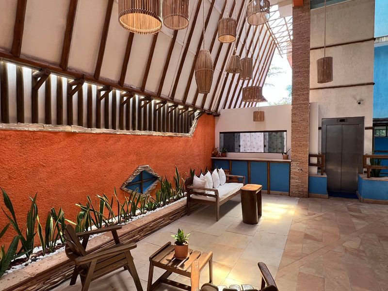 Uma área de estar externa com parede texturizada em tom laranja, móveis de madeira e luminárias decorativas suspensas.