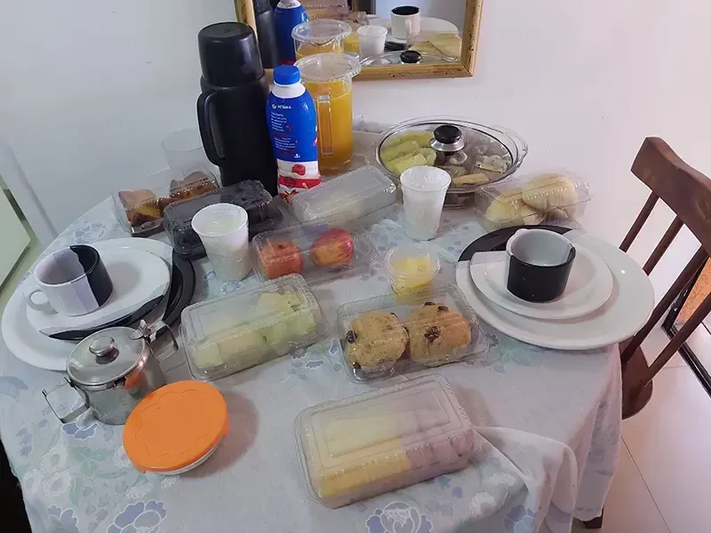 Café da manhã servido em uma mesa redonda, incluindo bebidas, pães e bolos, e diversos recipientes.