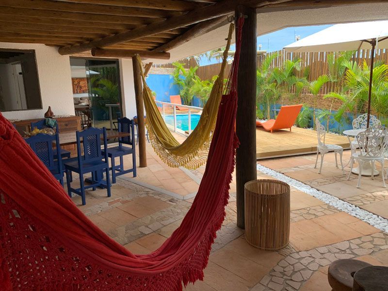 Pátio com redes, piscina e área de estar sob uma varanda sombreada.