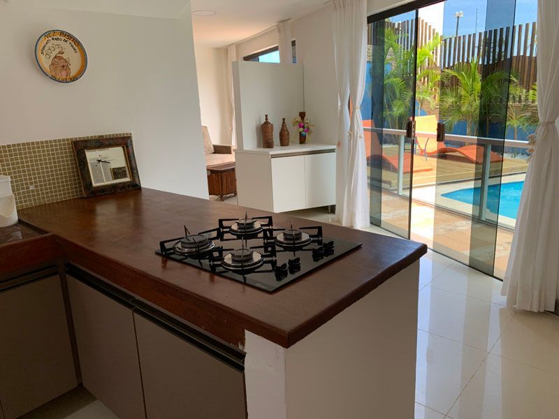 Cozinha com fogão, bancada de madeira e porta de vidro deslizante para a área da piscina.