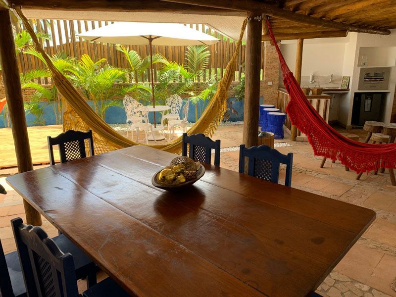 Mesa de madeira com cadeiras azuis em um pátio com redes e um jardim.