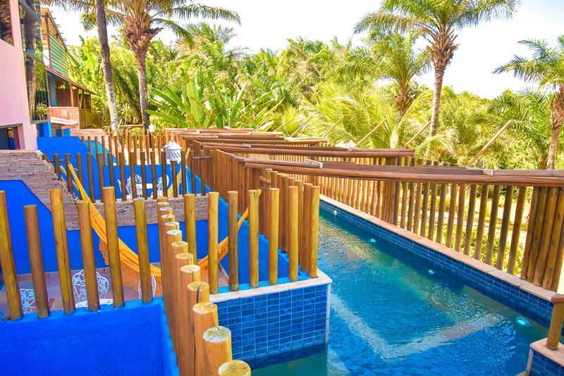 Piscinas revestidas com azulejos azuis e grades de madeira, ladeadas por palmeiras.