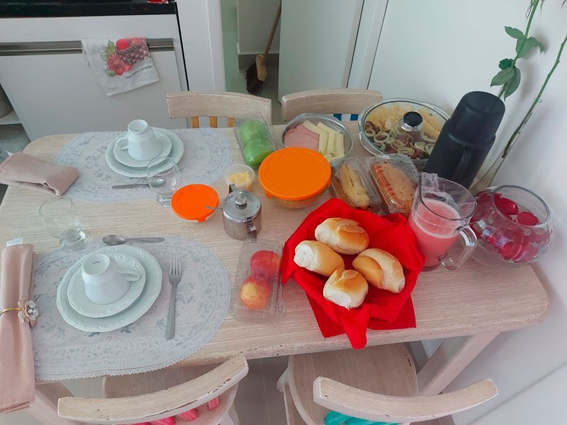 Mesa de café da manhã posta com pratos, pão, frutas e bebidas.