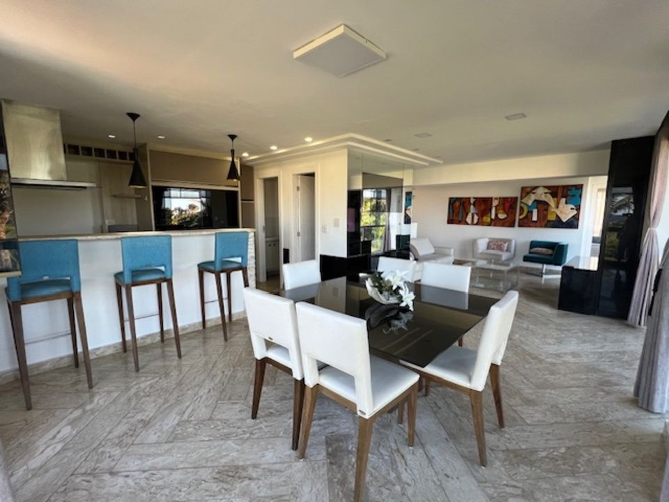 Espaço aberto com área de jantar, balcão de cozinha com banquetas azuis e área de estar com obras de arte.