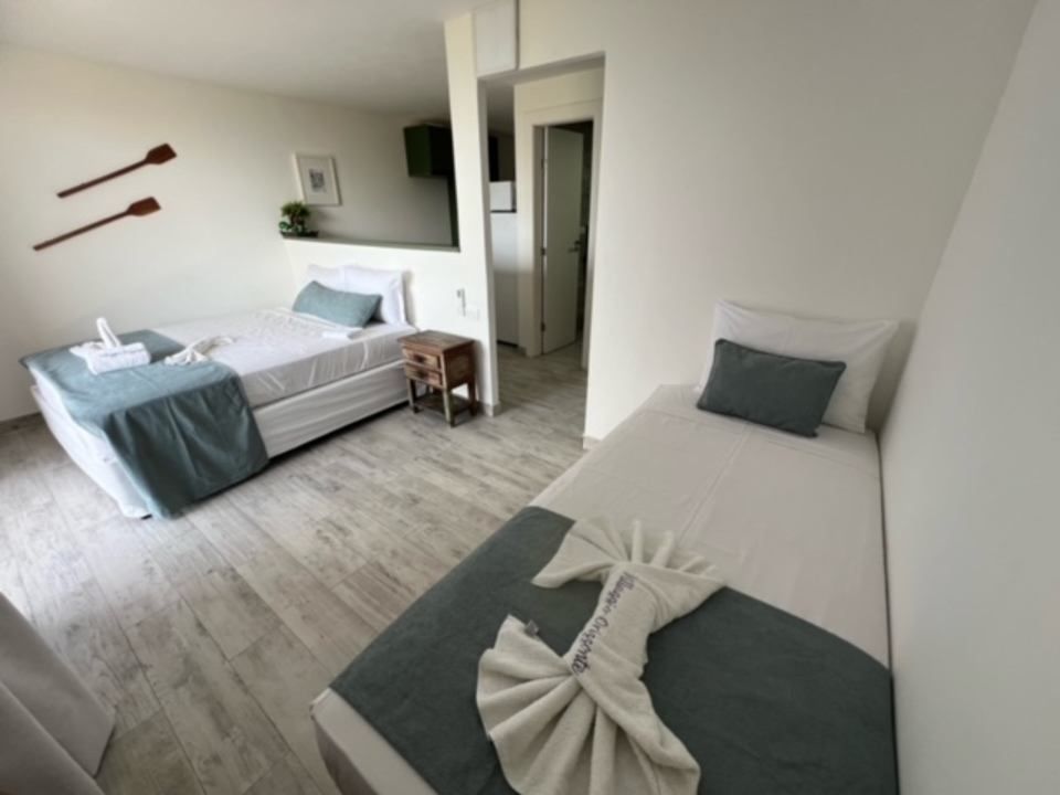 Duas camas em um quarto com paredes brancas, detalhes em cinza e piso de madeira. A roupa de cama é decorada com arte feita de toalhas.