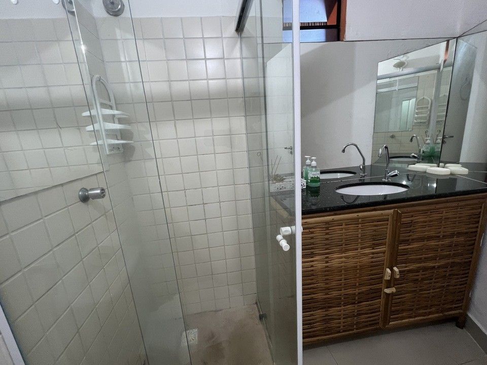 Banheiro com box de chuveiro à esquerda e pia com espelho à direita.