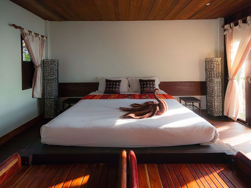 Quarto com cama grande, plataforma de madeira e luz natural. Toalha em formato de cisne sobre a cama.