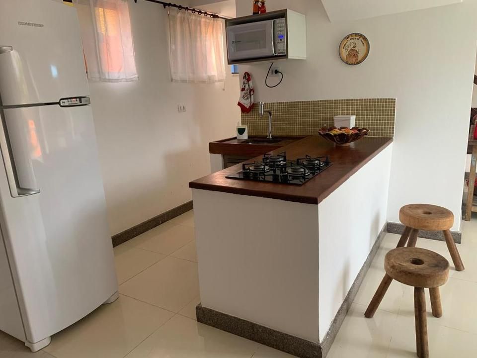 Cozinha pequena com geladeira branca, balcão com fogão e banquetas de madeira.