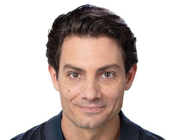 Man with dark hair and brown eyes smiling against a white background.