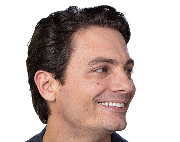 Smiling man with dark hair and skin looking right, wearing a dark top, on a white background.
