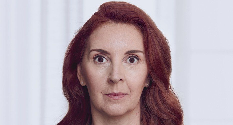 Woman with red hair looking directly at the camera; neutral expression; light background.