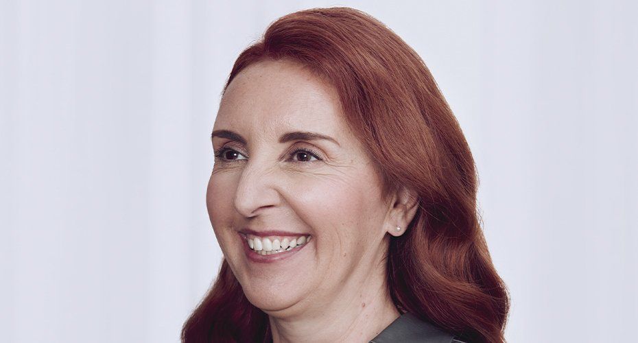 Woman with auburn hair smiles widely, looking to the side, against a white backdrop.
