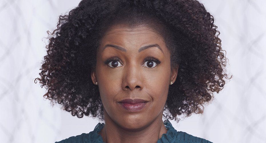 Woman with curly dark hair, surprised expression, looking forward. Teal top, light background.