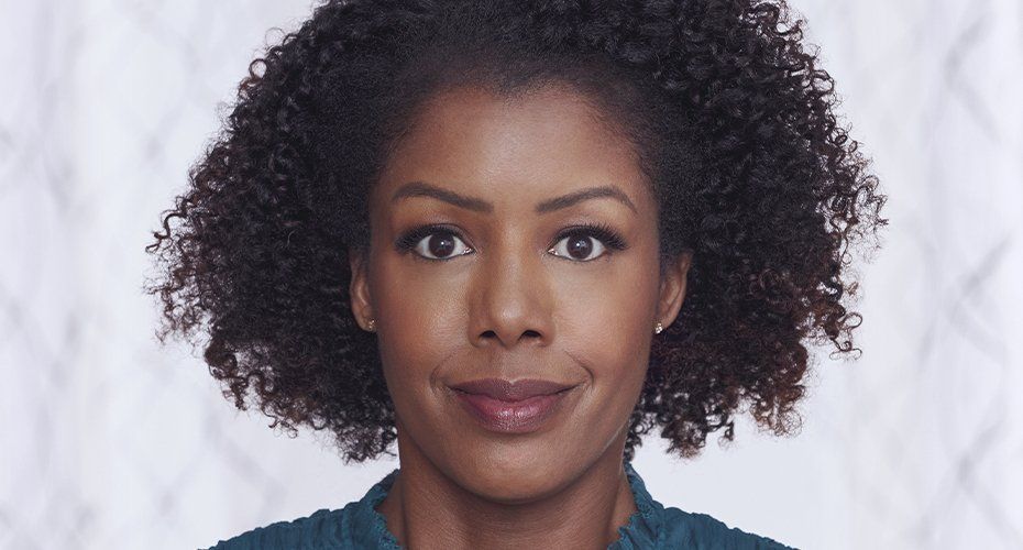 Woman with dark curly hair, smiling at the camera, wearing a teal top.