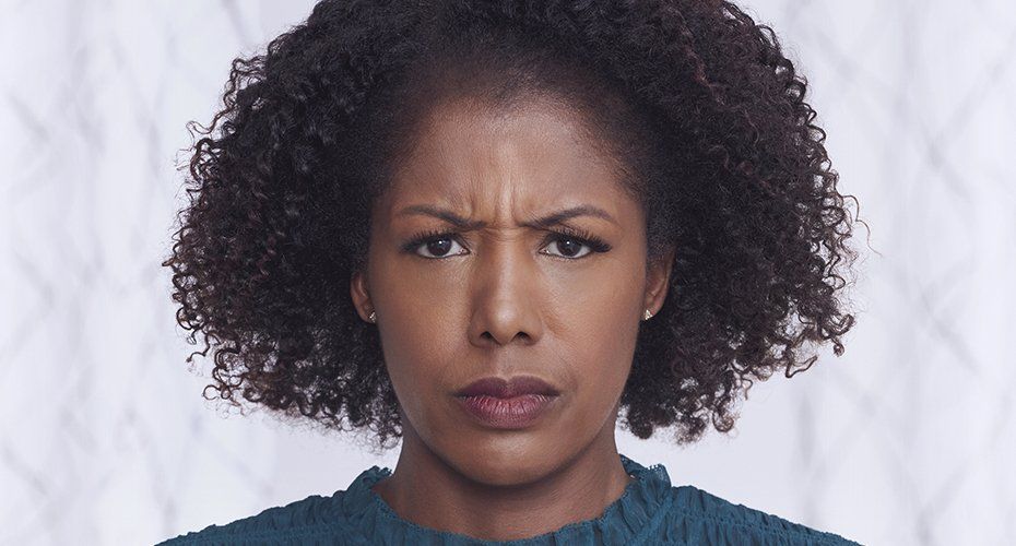 A Black woman with curly hair frowns, looking directly at the camera with furrowed brows.