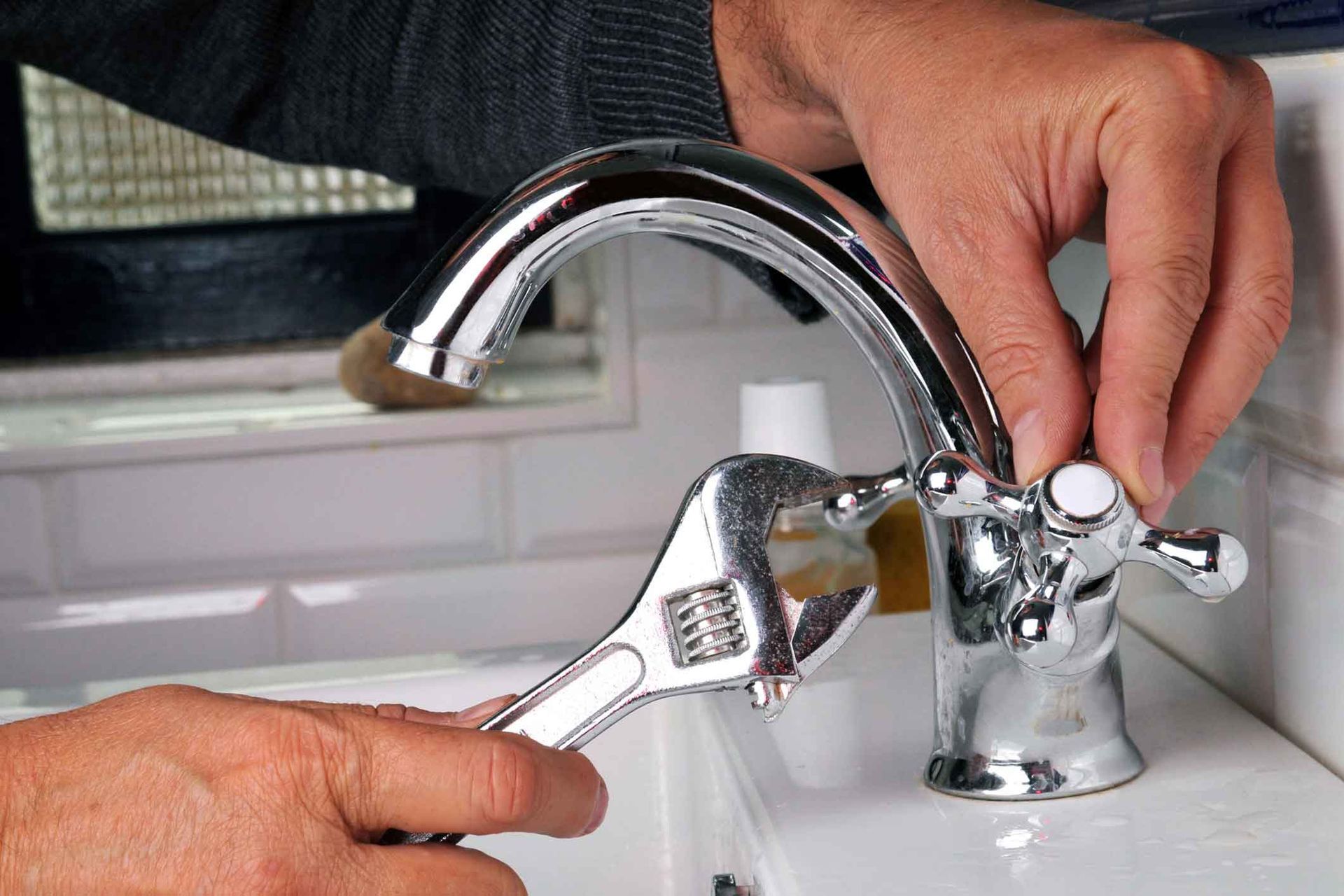 A man is fixing a sink faucet with a wrench.