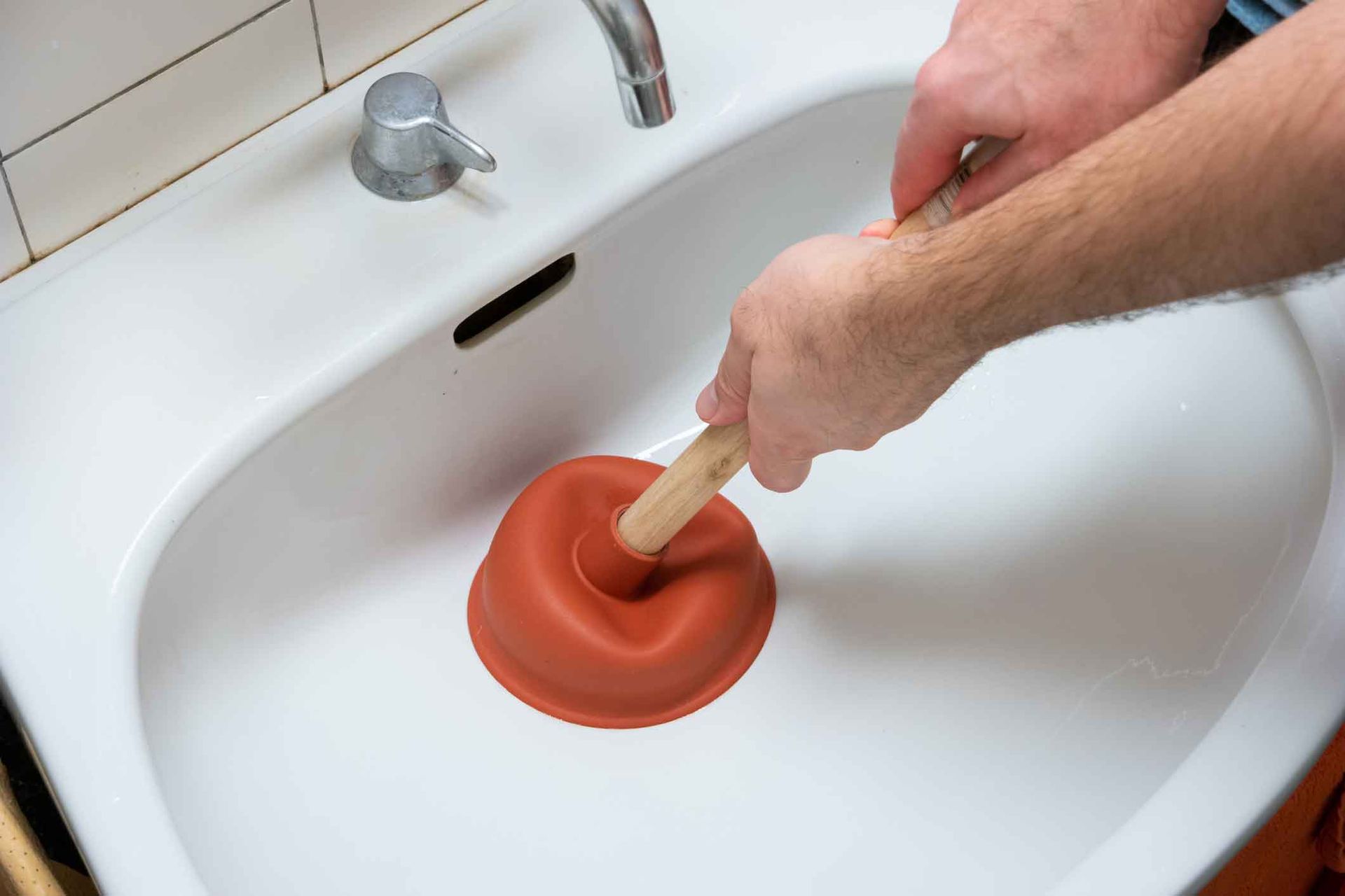 A person is using a plunger to unblock a sink.