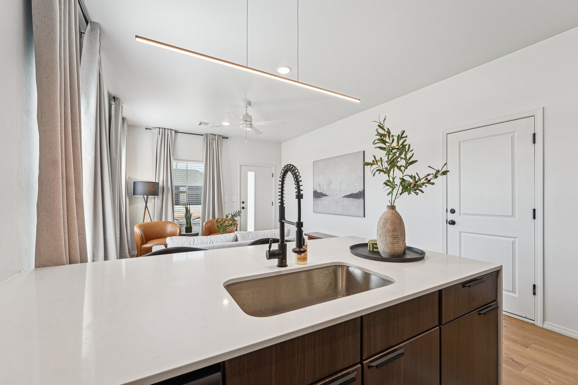 Modern kitchen island with sink, dark cabinets, and white countertop, with view into a living space.