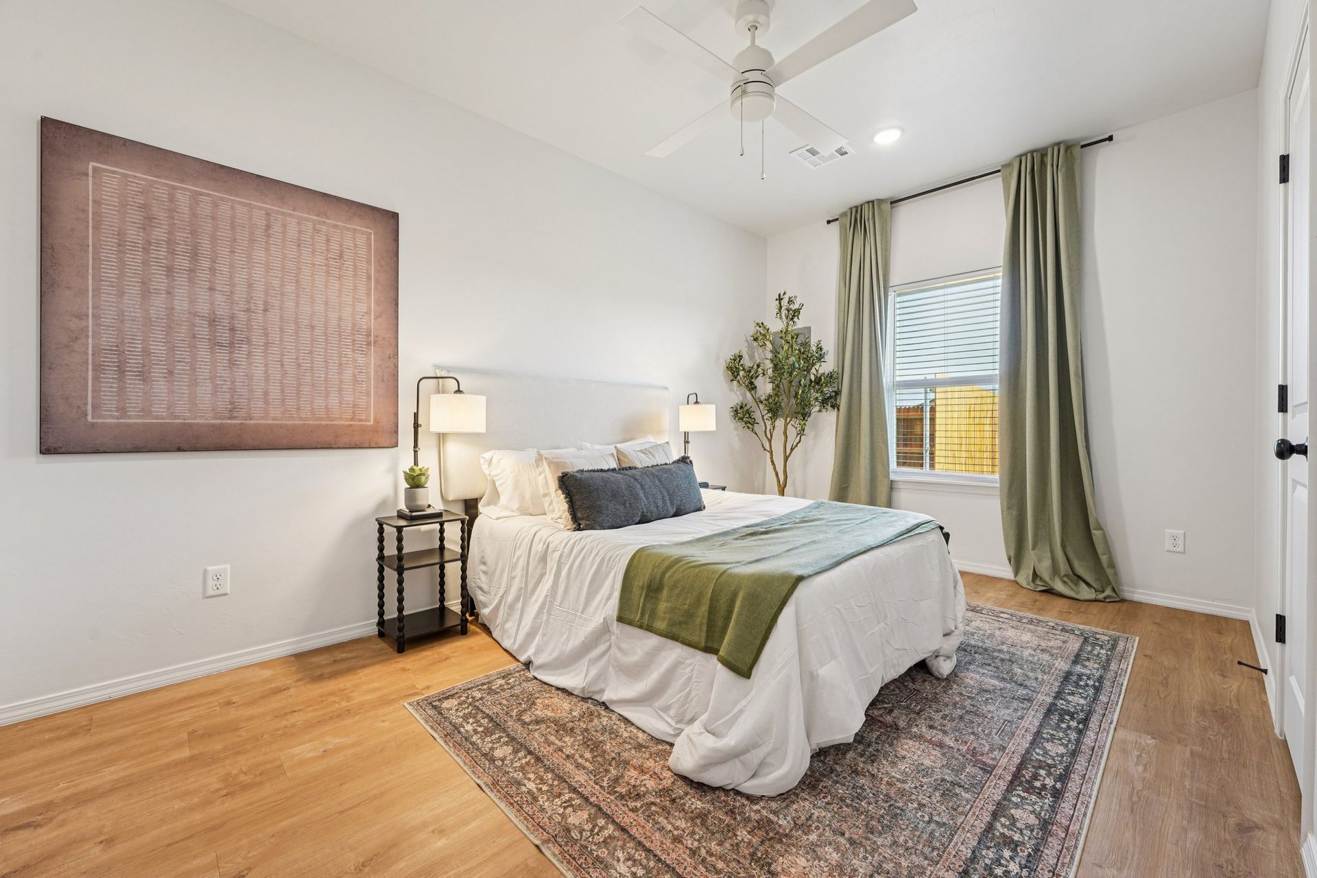 Bedroom with a bed, nightstand, artwork, rug, green curtains, and a ceiling fan.