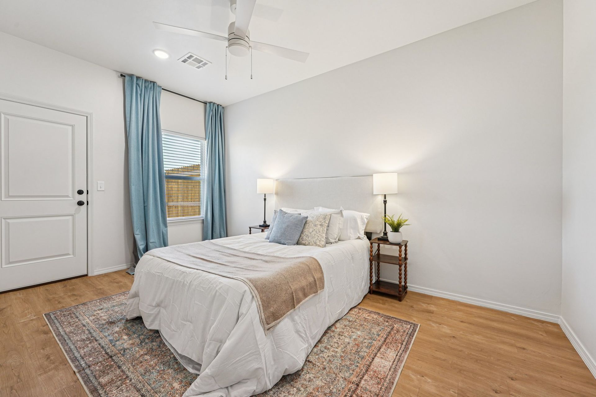 Bedroom with bed, blue curtains, wooden floor, and a rug.