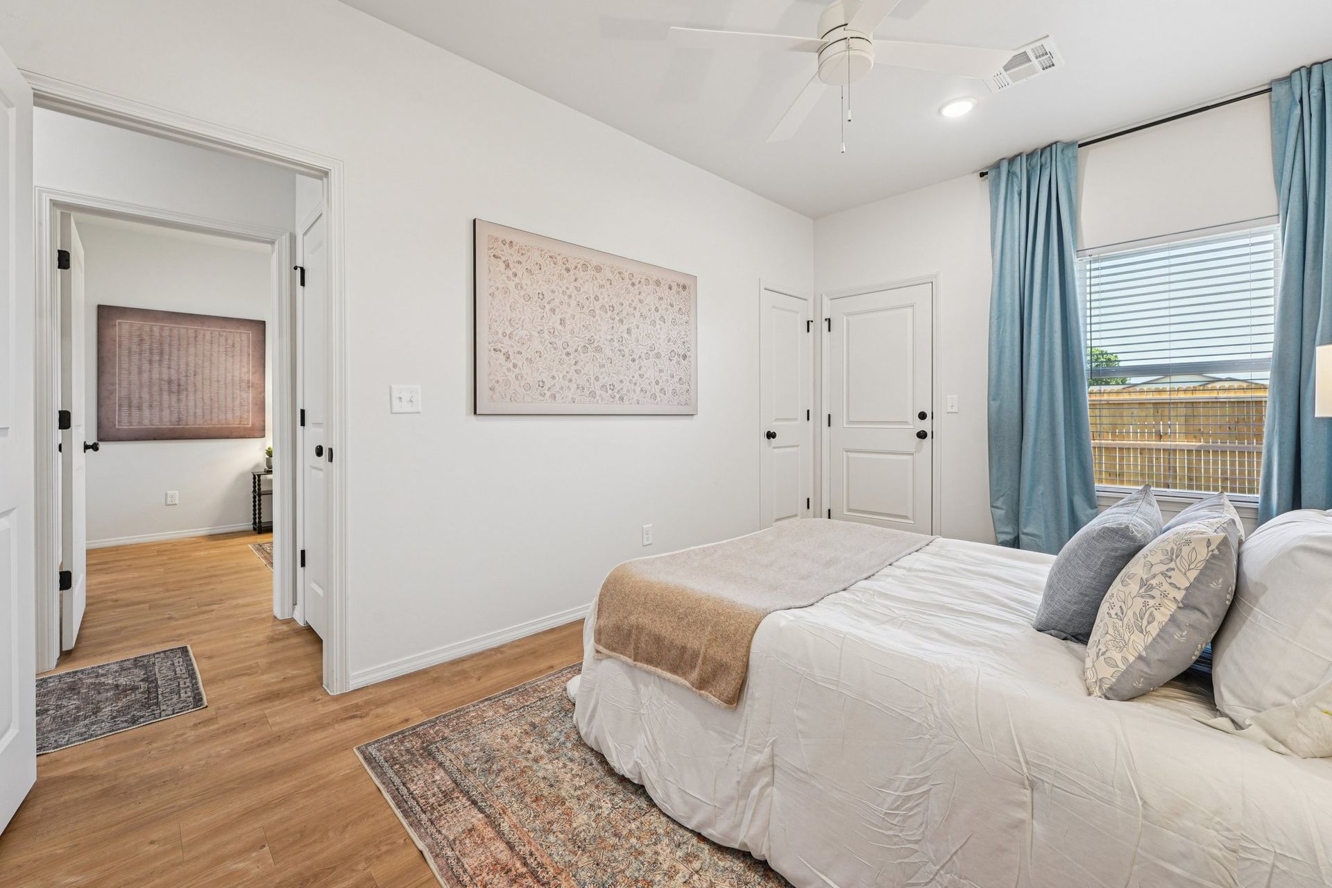 Bedroom with white walls, a bed with light bedding, blue curtains, and a rug.