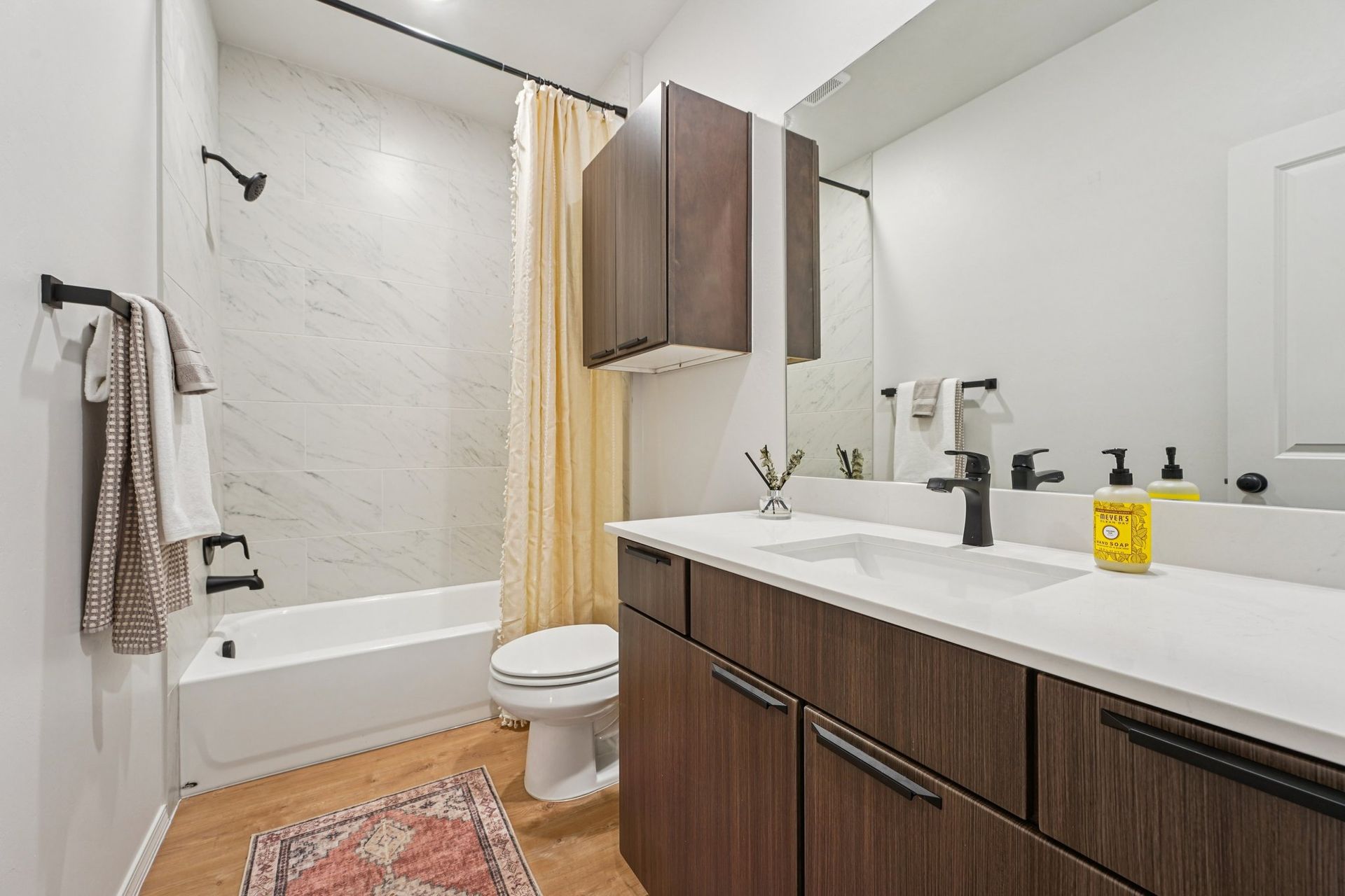 Bathroom with white countertop, dark wood cabinets, and marble-look shower surround.