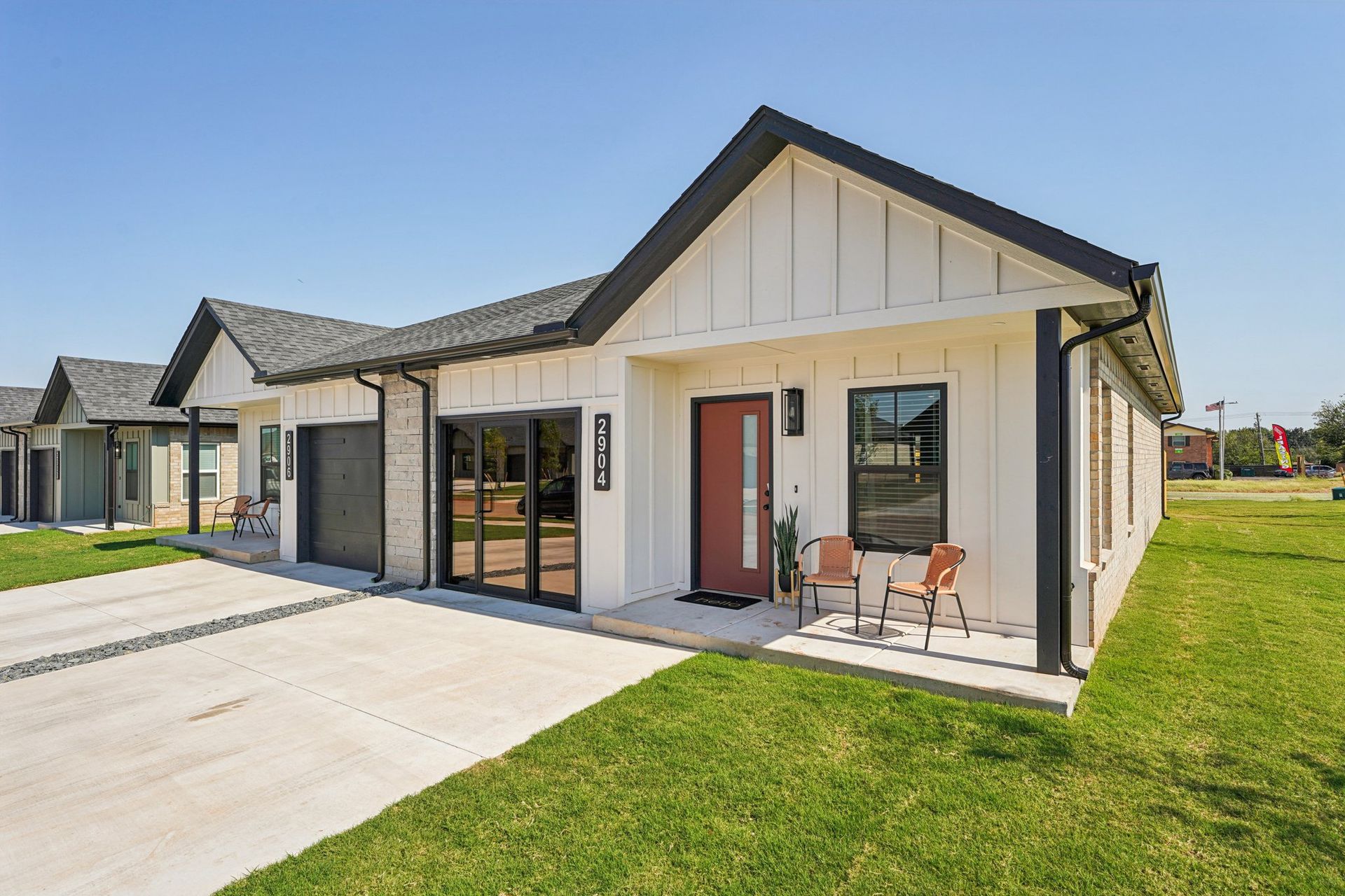 White modern houses with black trim, concrete driveways, and green lawns on a sunny day.
