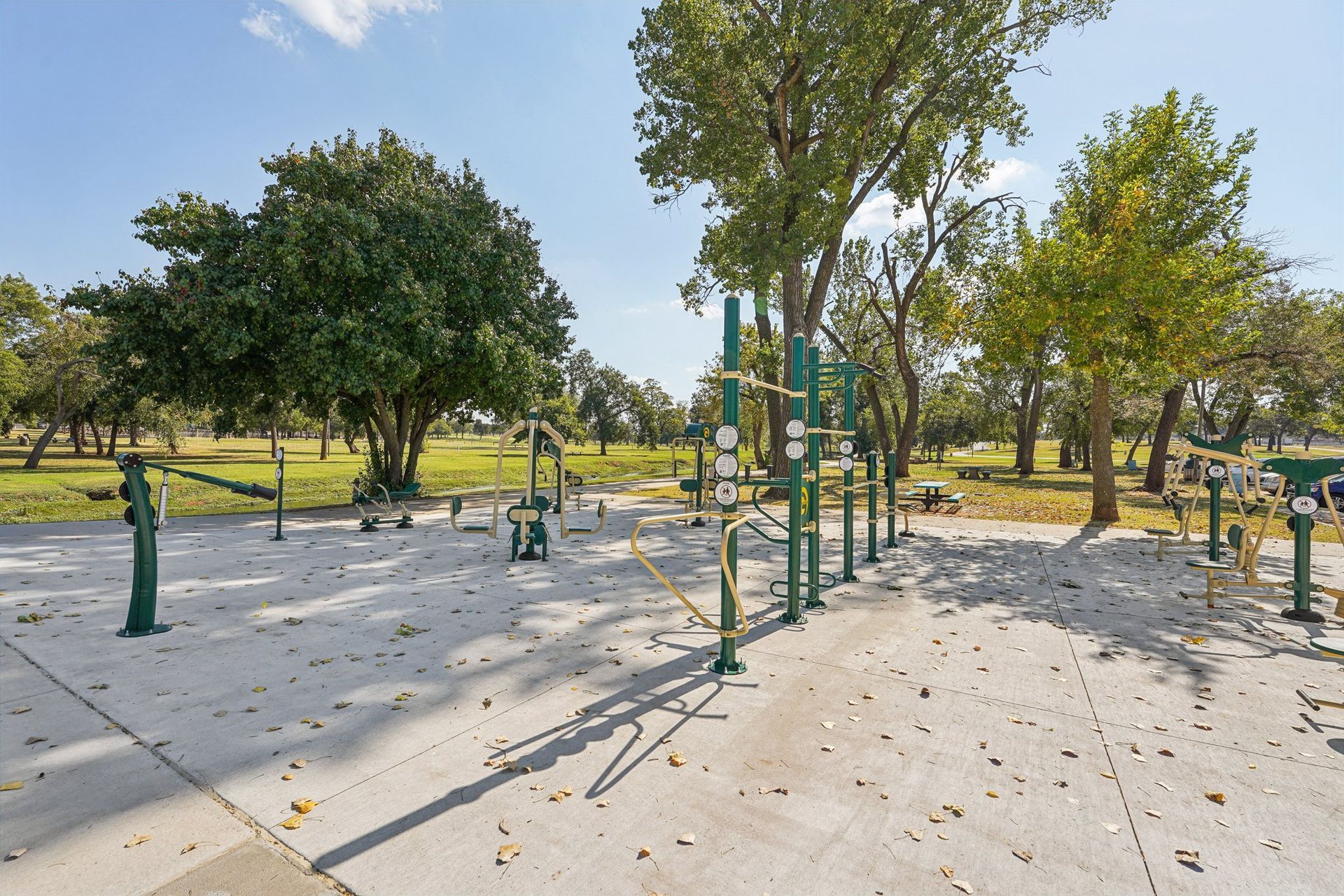 Outdoor exercise equipment in a park, with green structures on a concrete surface. Trees in the background.