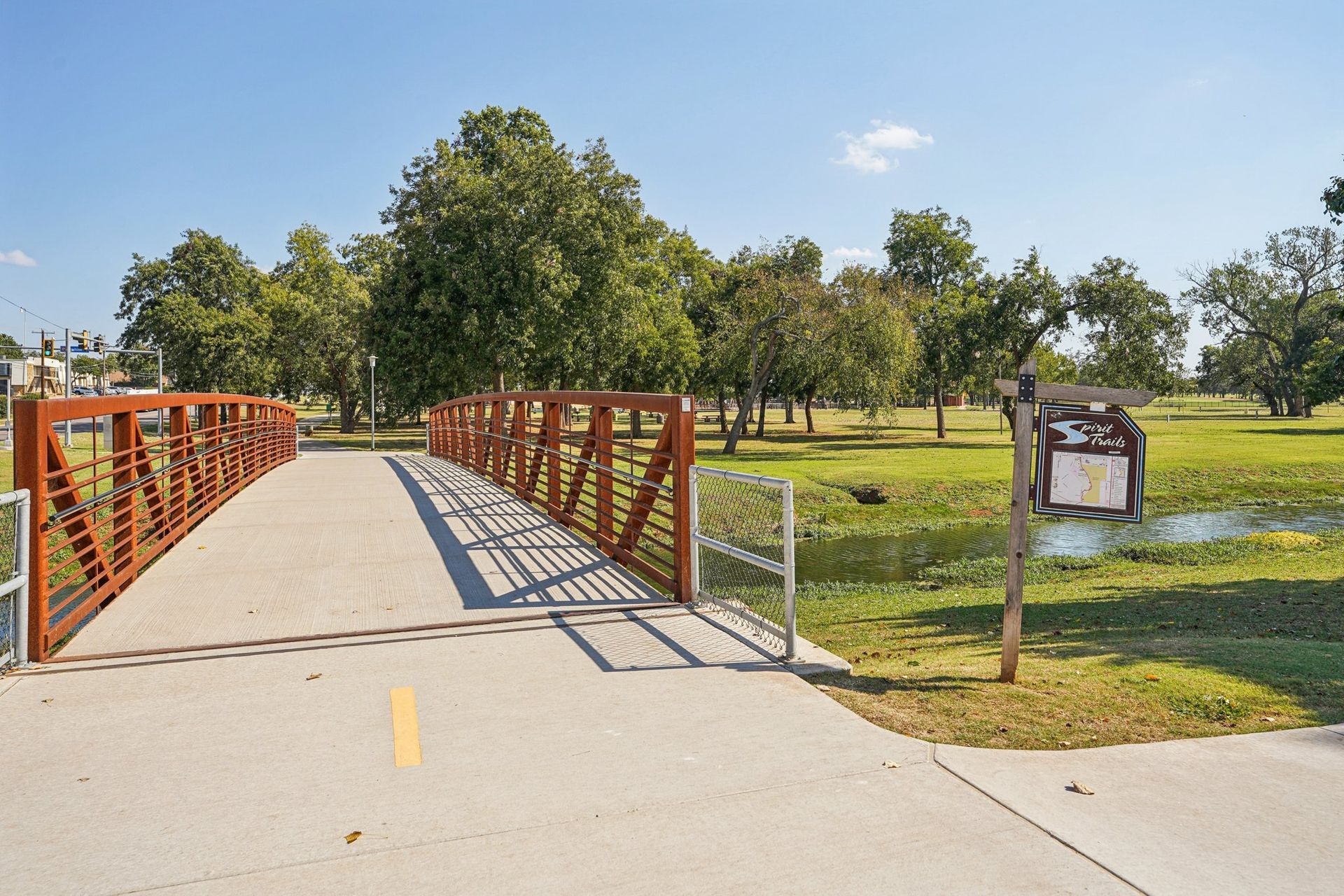 Bridge over a grassy area with trees and a sign on a sunny day.