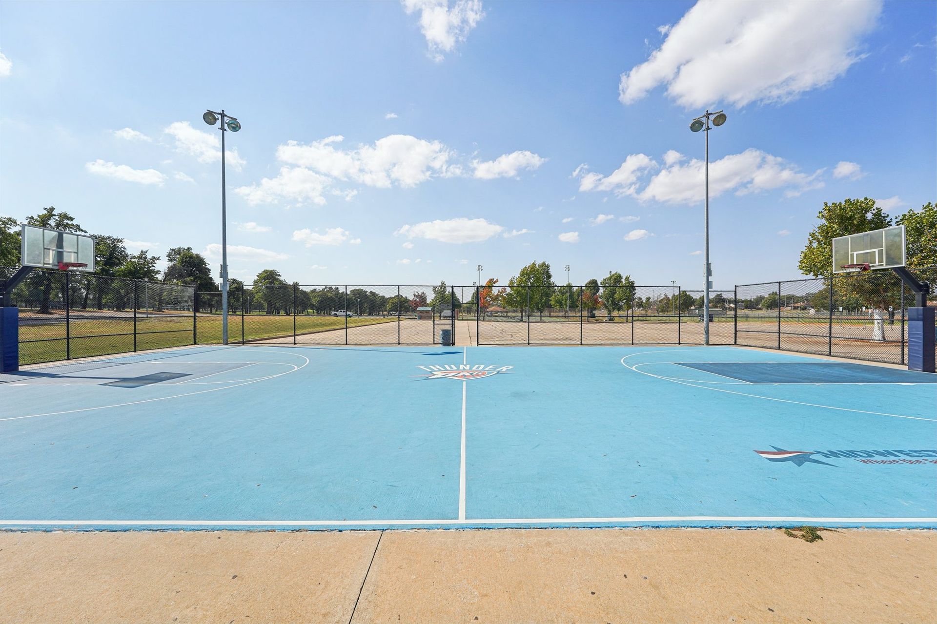 Blue outdoor sports court with basketball hoops and a volleyball net under a blue sky.