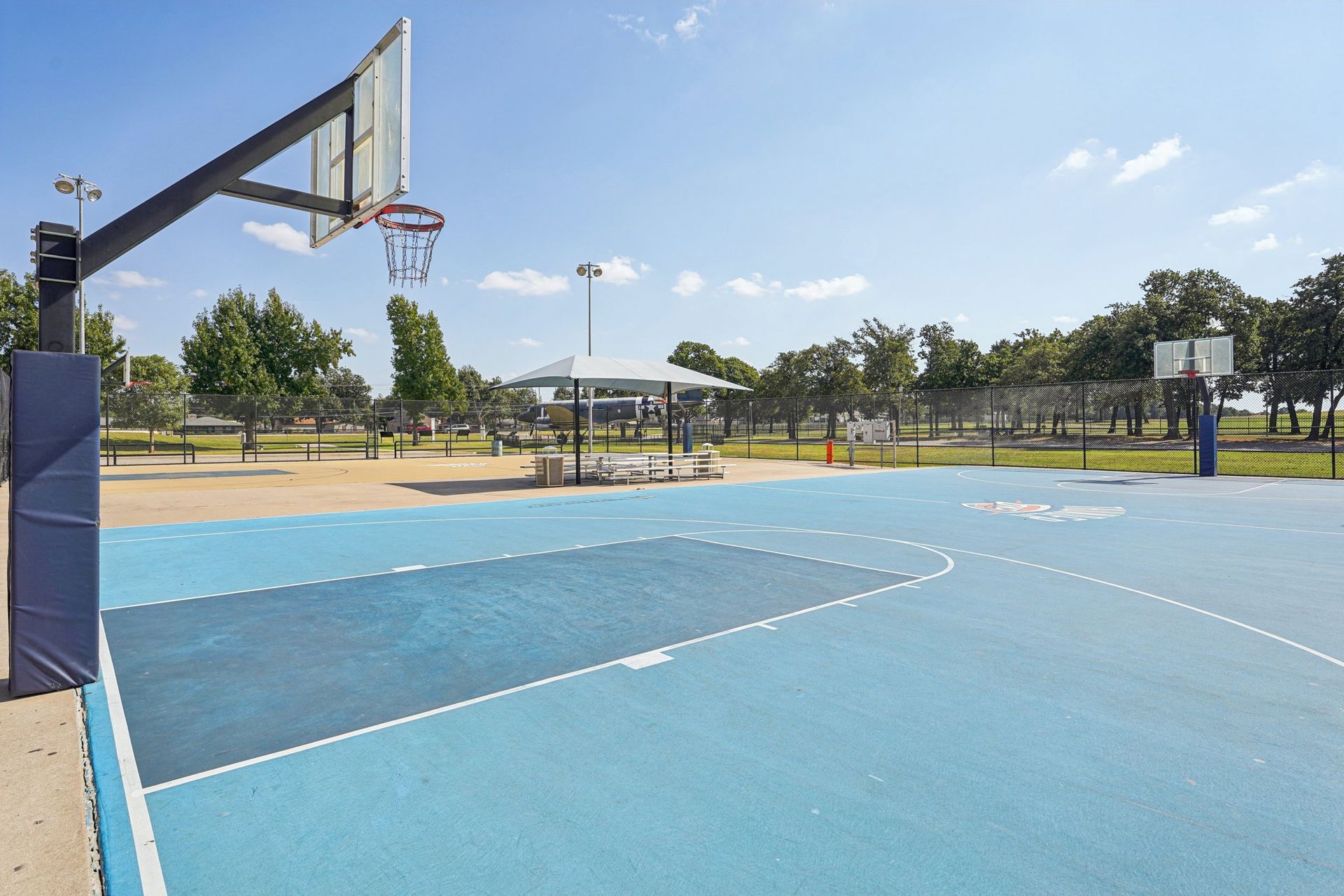 Basketball court with blue surface and white lines under a clear sky.