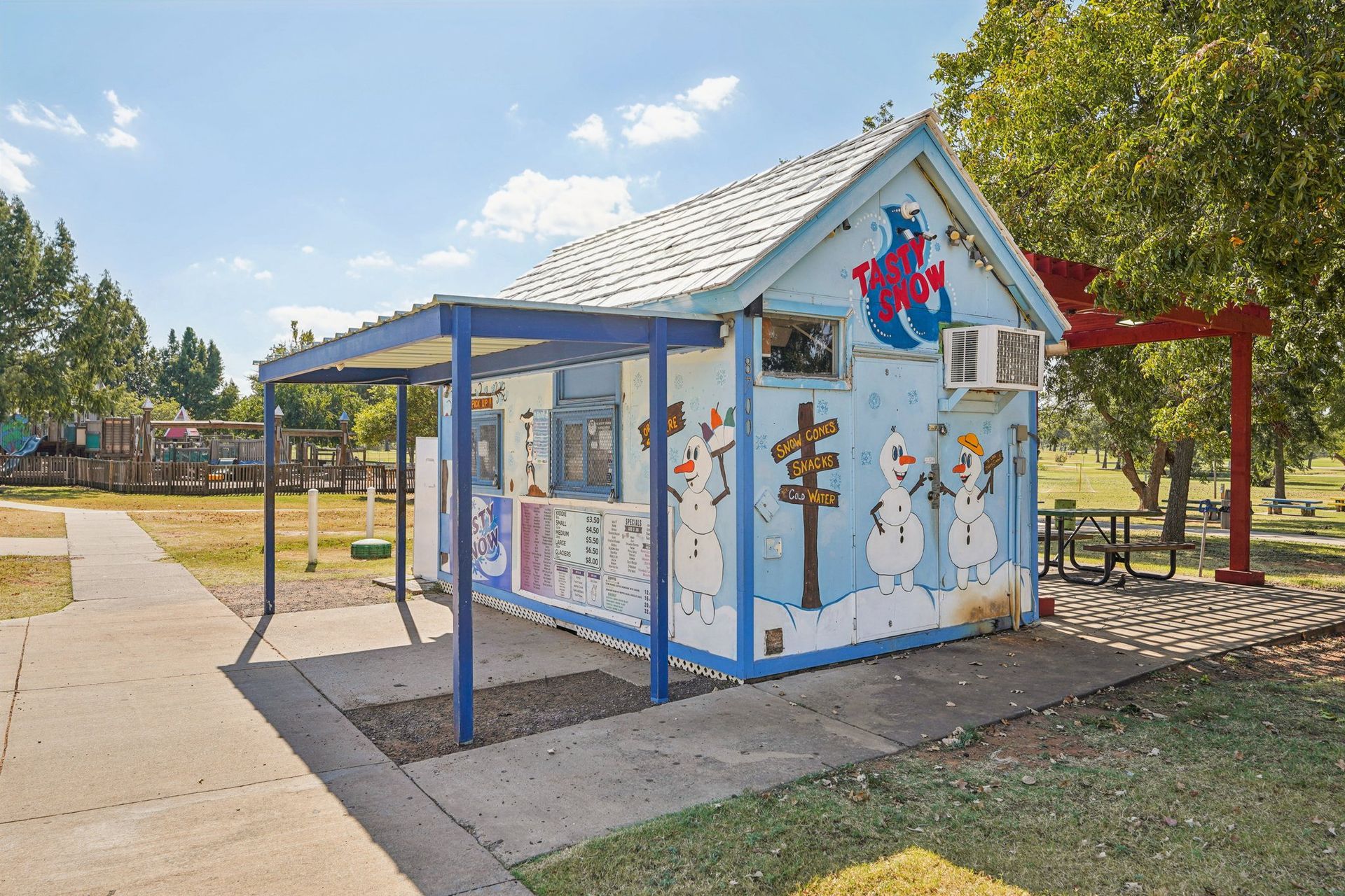 Blue and white painted snack shack with snowman mural and awning.