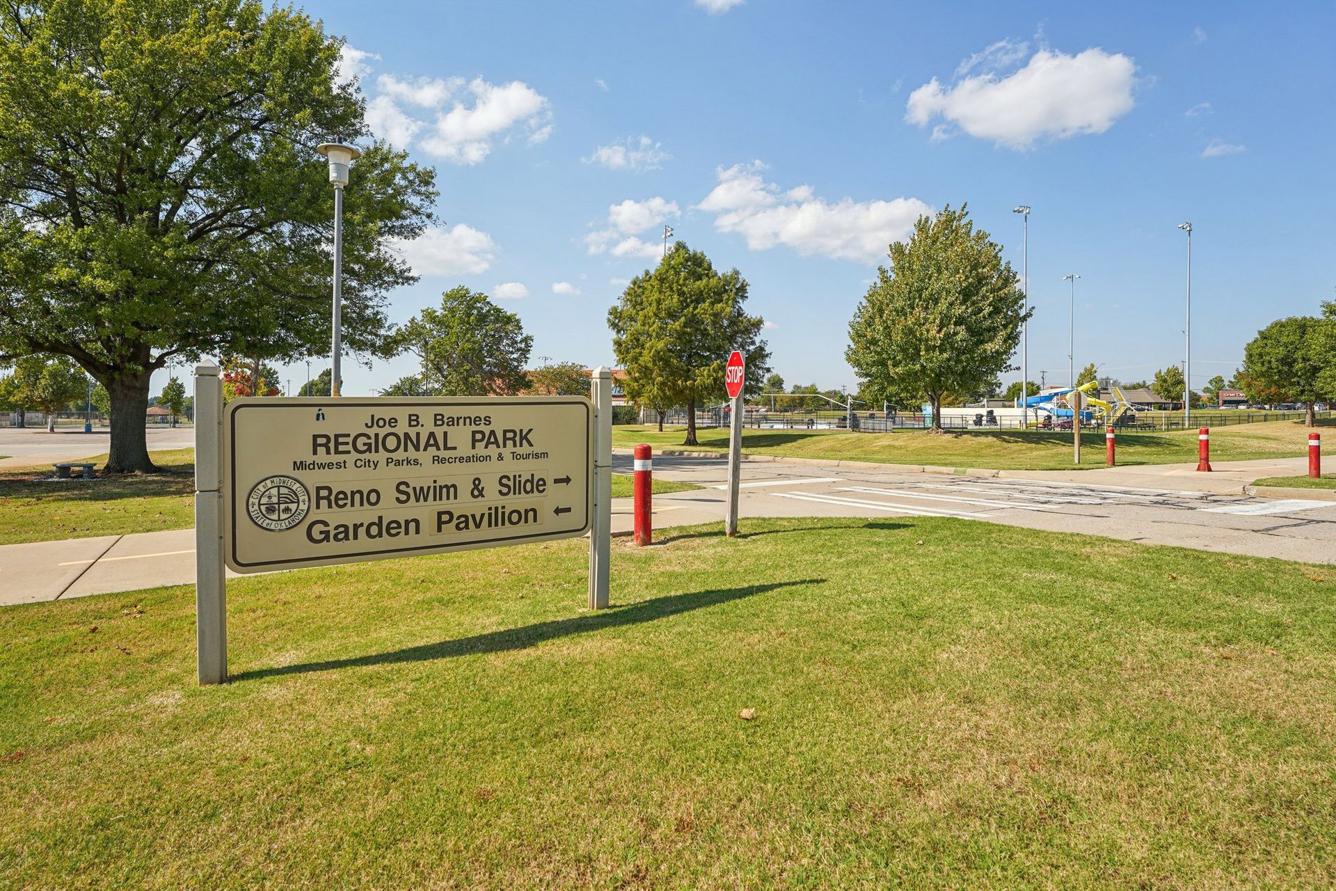 Sign for John P. Parks Regional Park; grassy area, trees, paved path, cloudy sky.