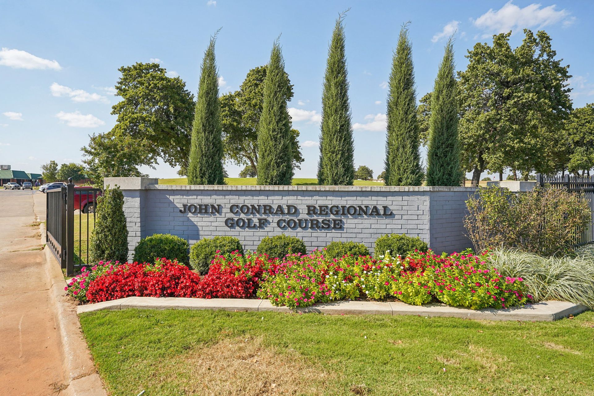 Sign for John Conrad Regional Golf Course with landscaping, trees, and bright red flowers.