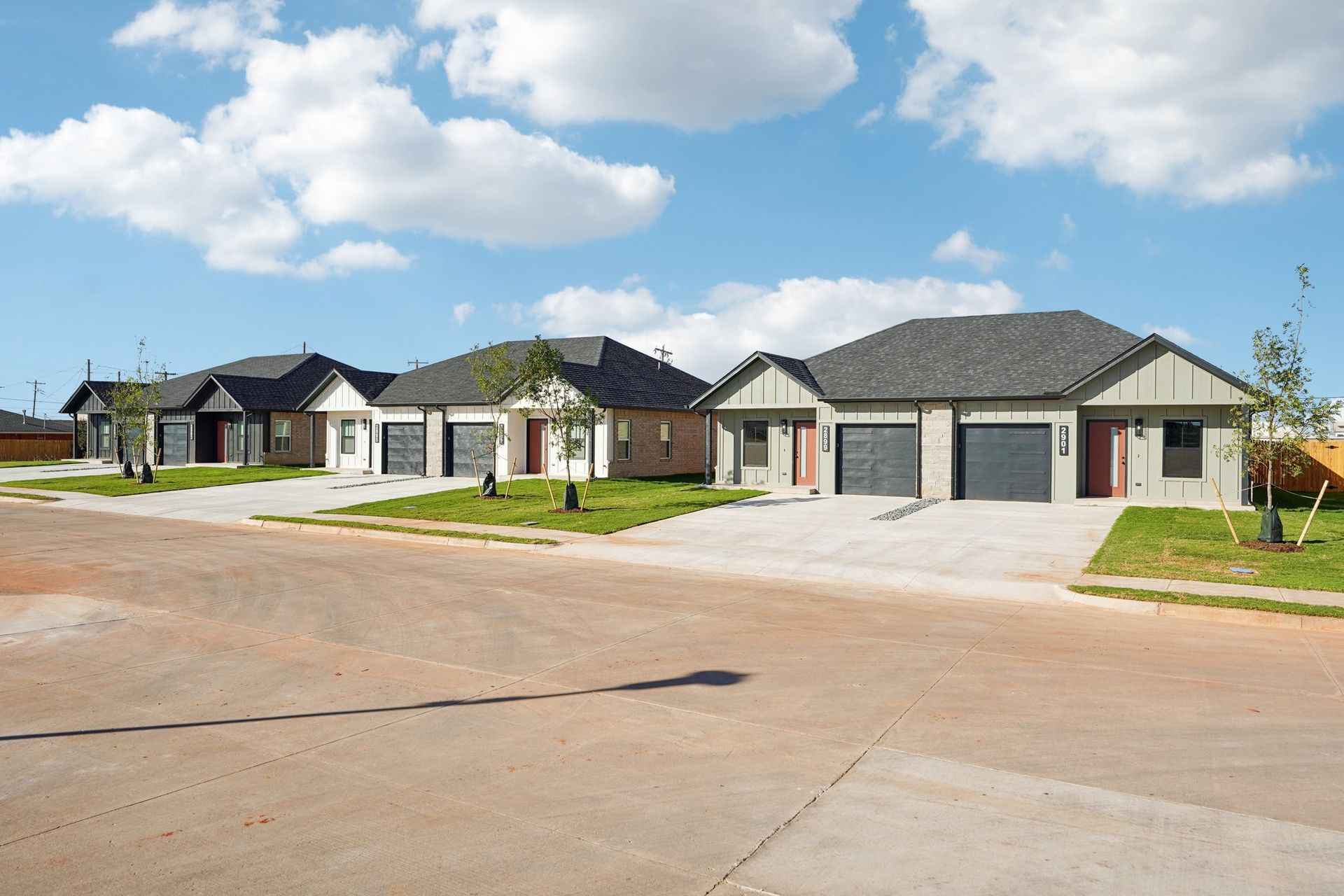 Row of modern houses with gray roofs and garages on a sunny street.