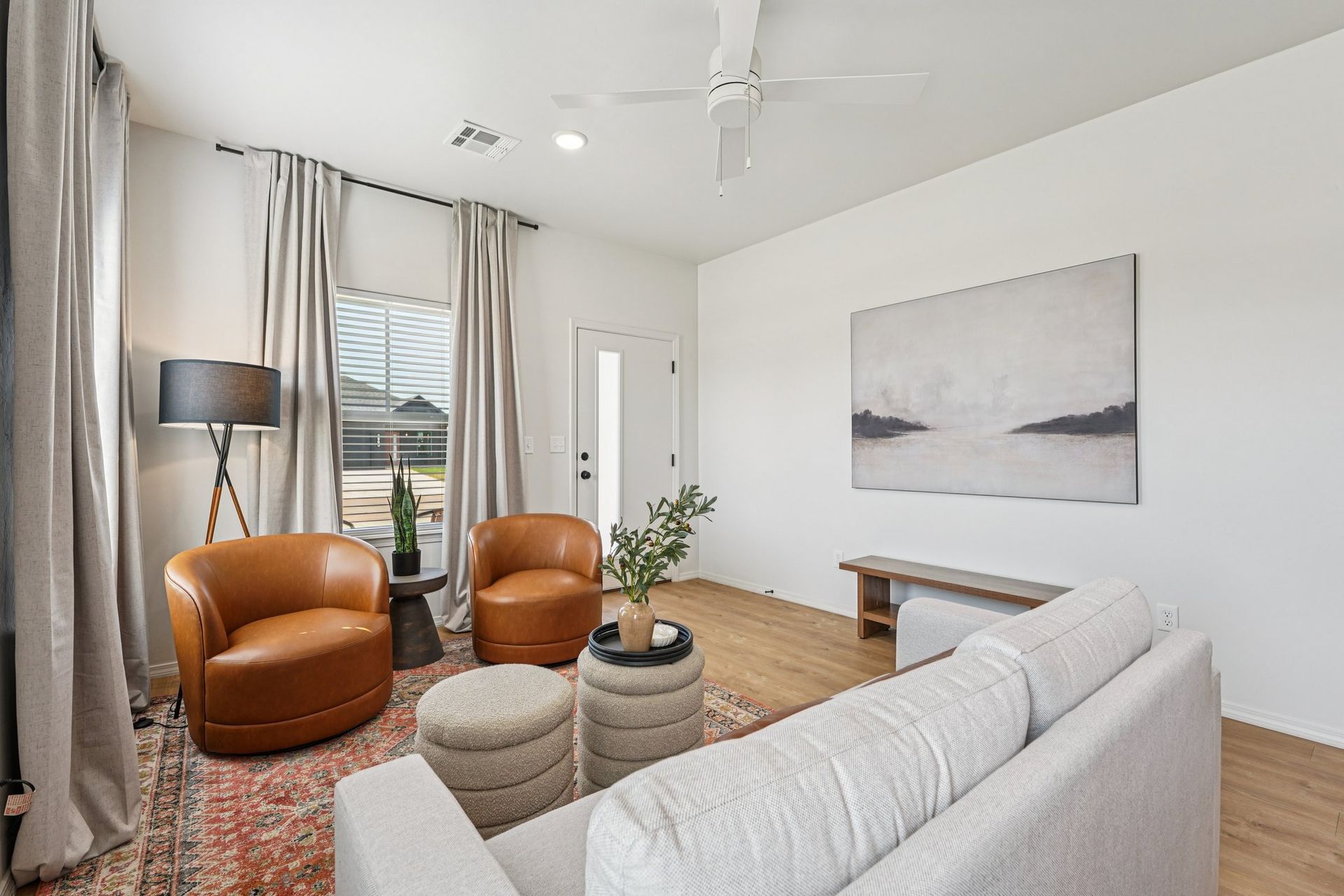 Living room with light-colored walls, wood floors, neutral furniture, and a landscape painting.