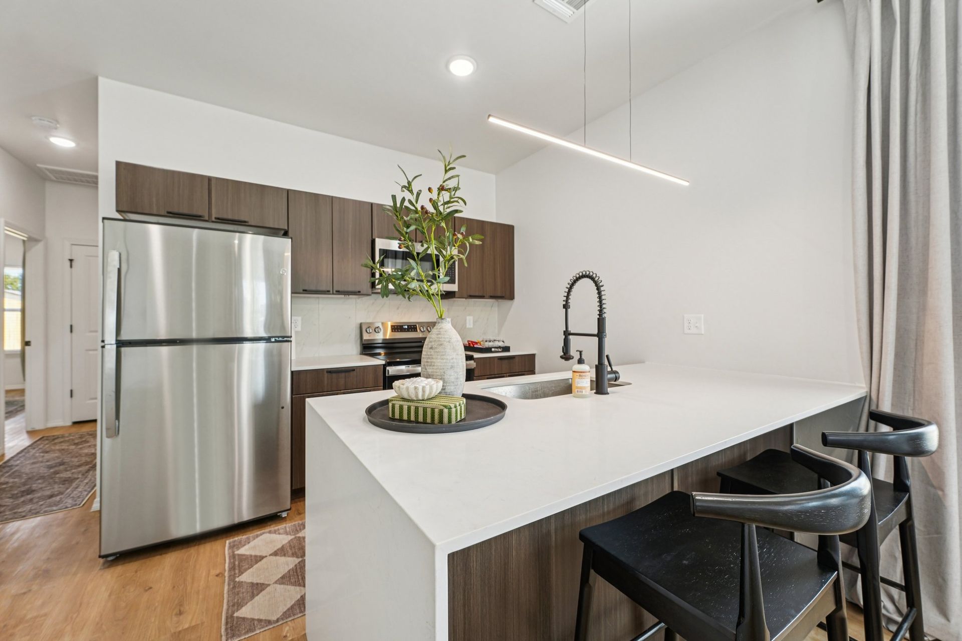 Modern kitchen with stainless steel appliances, dark wood cabinets, white countertops, and a breakfast bar with stools.