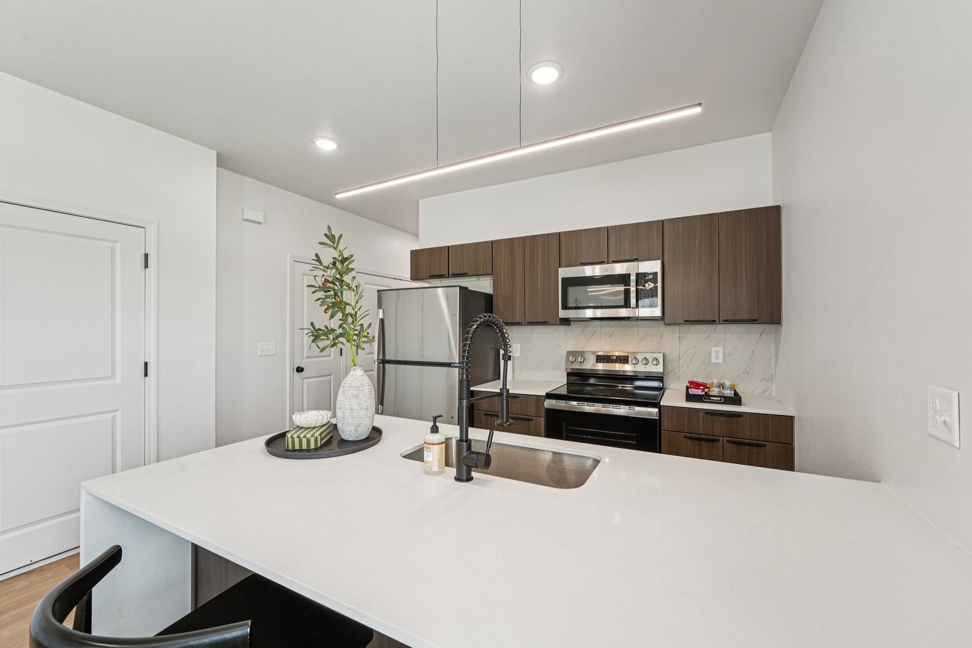Modern kitchen with white countertops, dark wood cabinets, stainless steel appliances, and a central island with a sink.