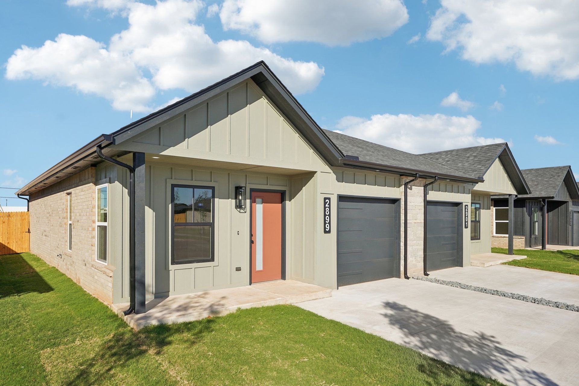 Row of attached modern homes with green siding, grey roofs, and concrete driveways.