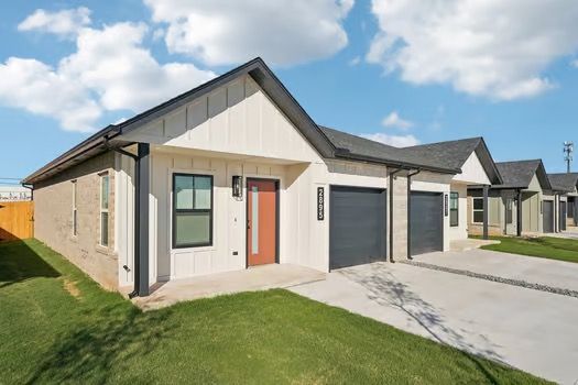 Row of modern townhomes with light brick, white siding, and black garage doors under a cloudy sky.