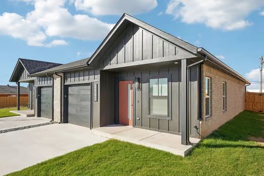 Modern gray duplex with garage, brick facade, and green lawn under a partly cloudy sky.