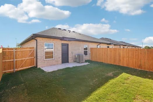 Backyard of a brick house with a wooden fence and green grass under a blue sky.