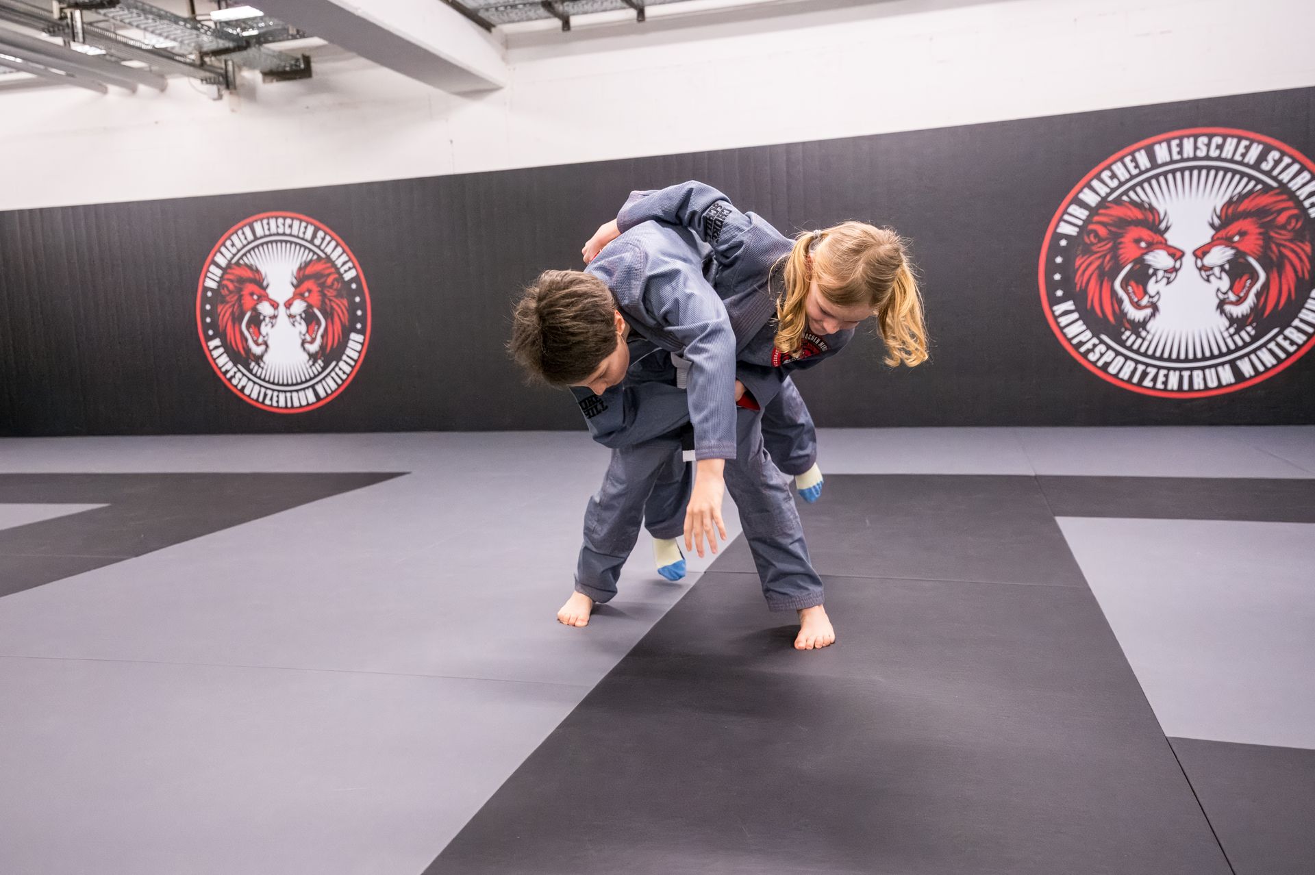 Ein Mann mit Bart bringt einem jungen Mann in einem Fitnessstudio Jiu-Jitsu bei.