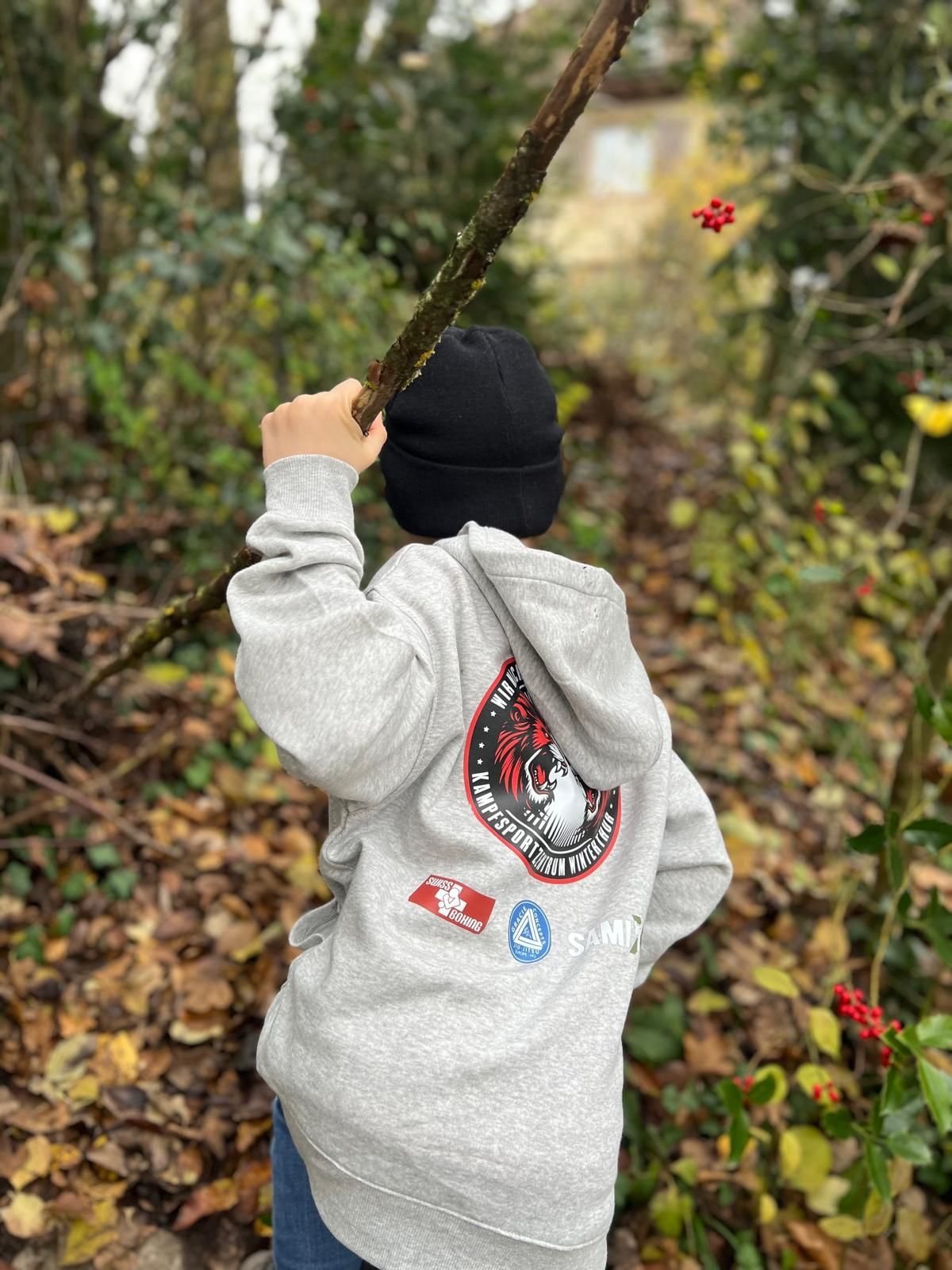 Ein kleiner Junge hält im Wald einen Stock.