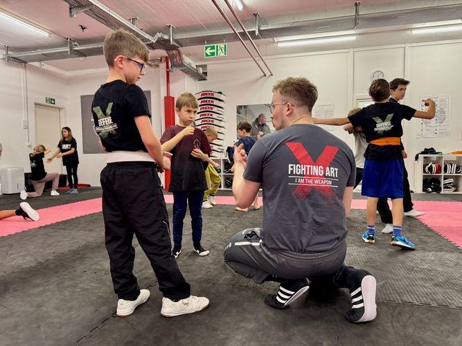 Ein Mann kniet in einer Turnhalle vor einer Gruppe von Kindern nieder.